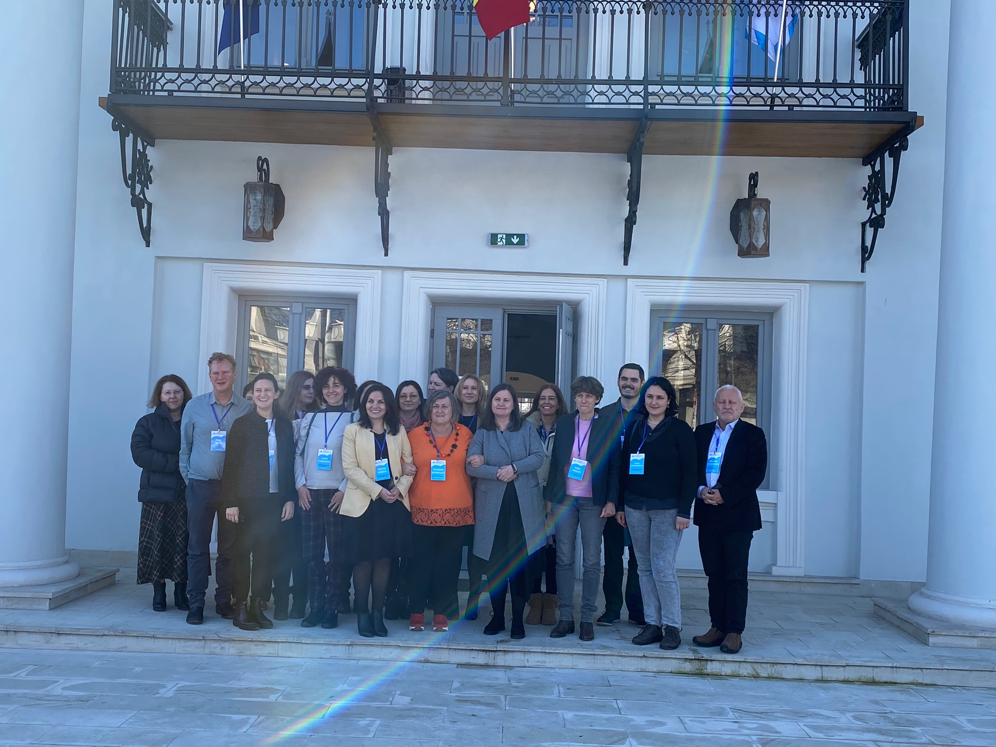 A group of people wearing lanyards pose for a photo in front of a white building.
